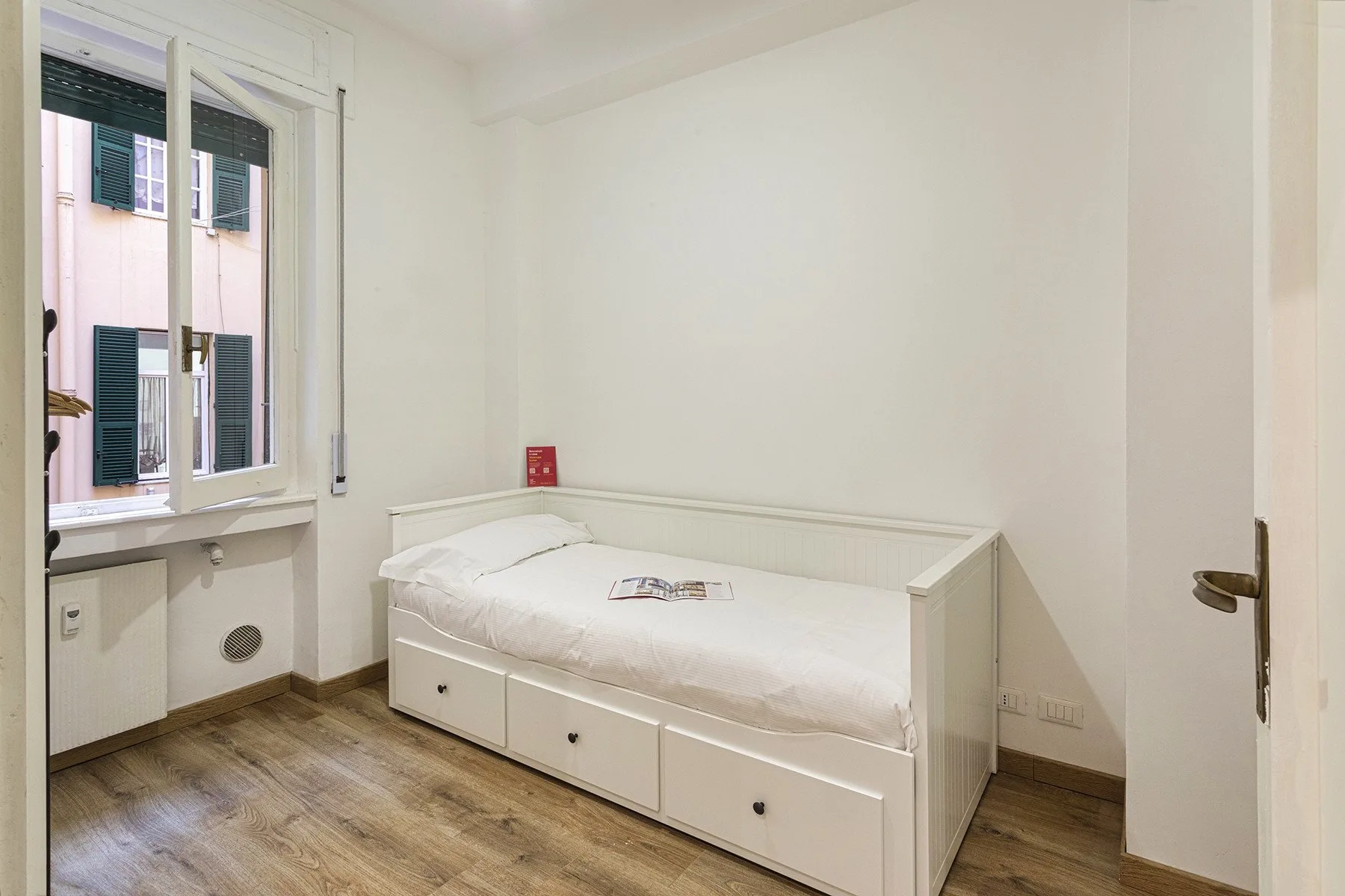 A simple bedroom with a white bed beneath a window.