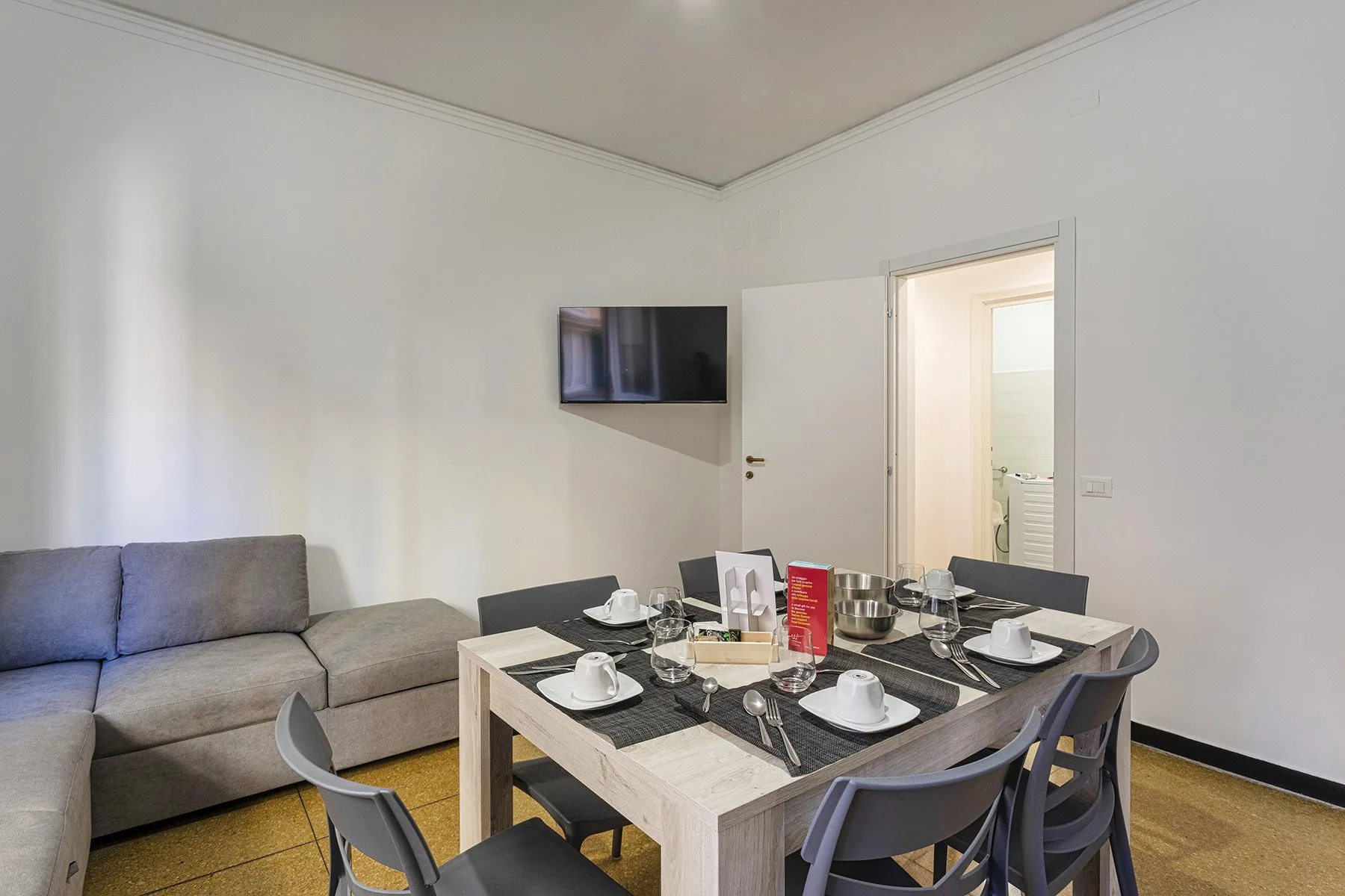 A dining area with a set table beside a gray sofa and wall-mounted television.