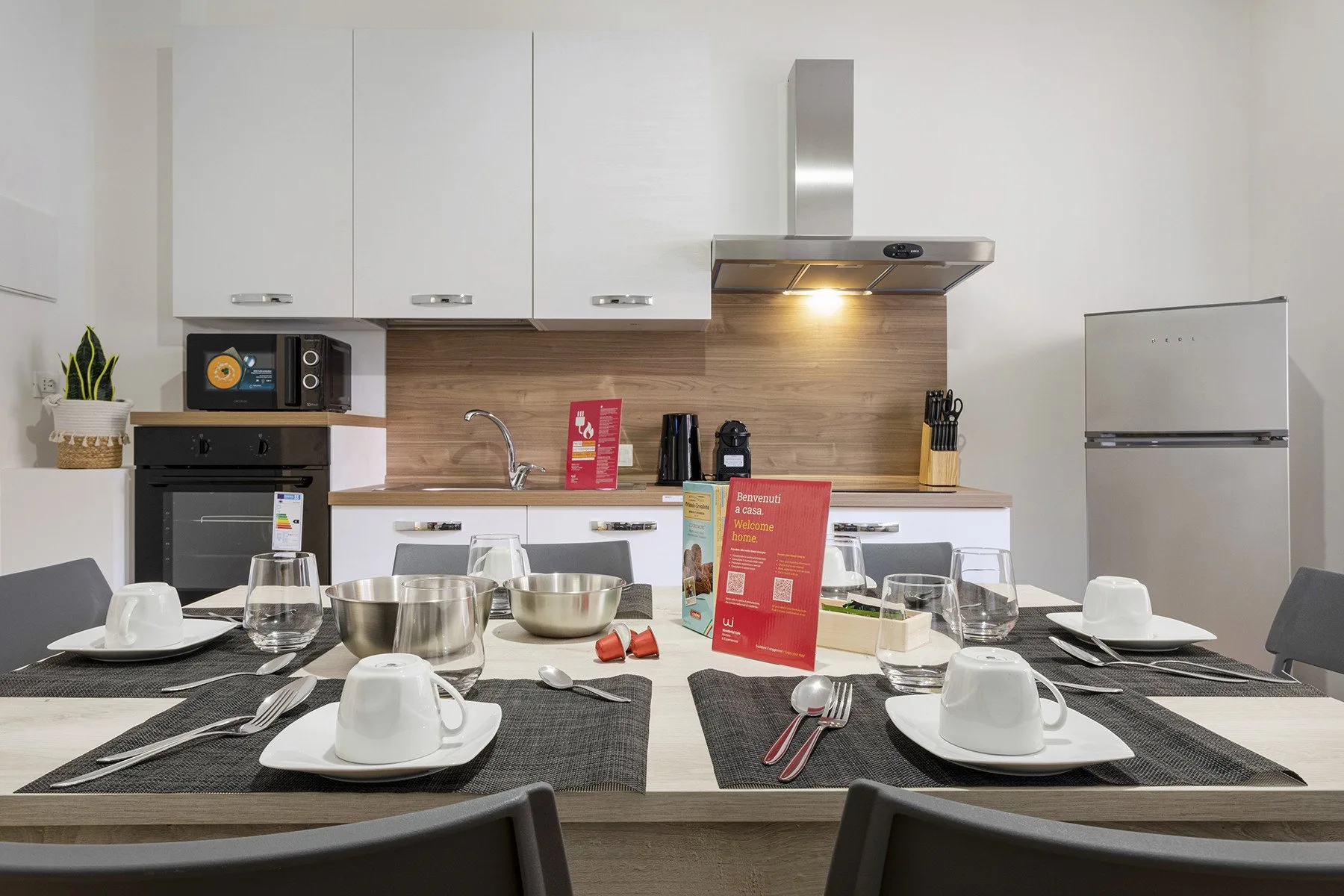 Una mesa está preparada frente a una cocina con gabinetes blancos.