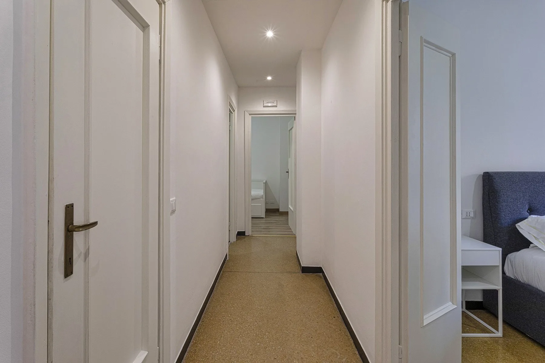 Un pasillo estrecho con varias puertas y un dormitorio visible al fondo.