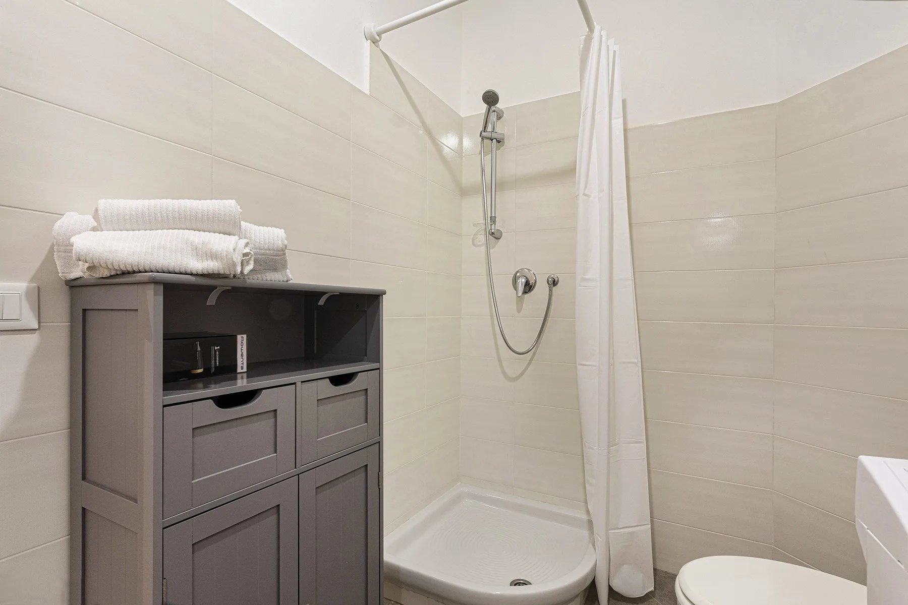 Un baño revestido de azulejos con ducha, mueble de almacenamiento y toallas dobladas.