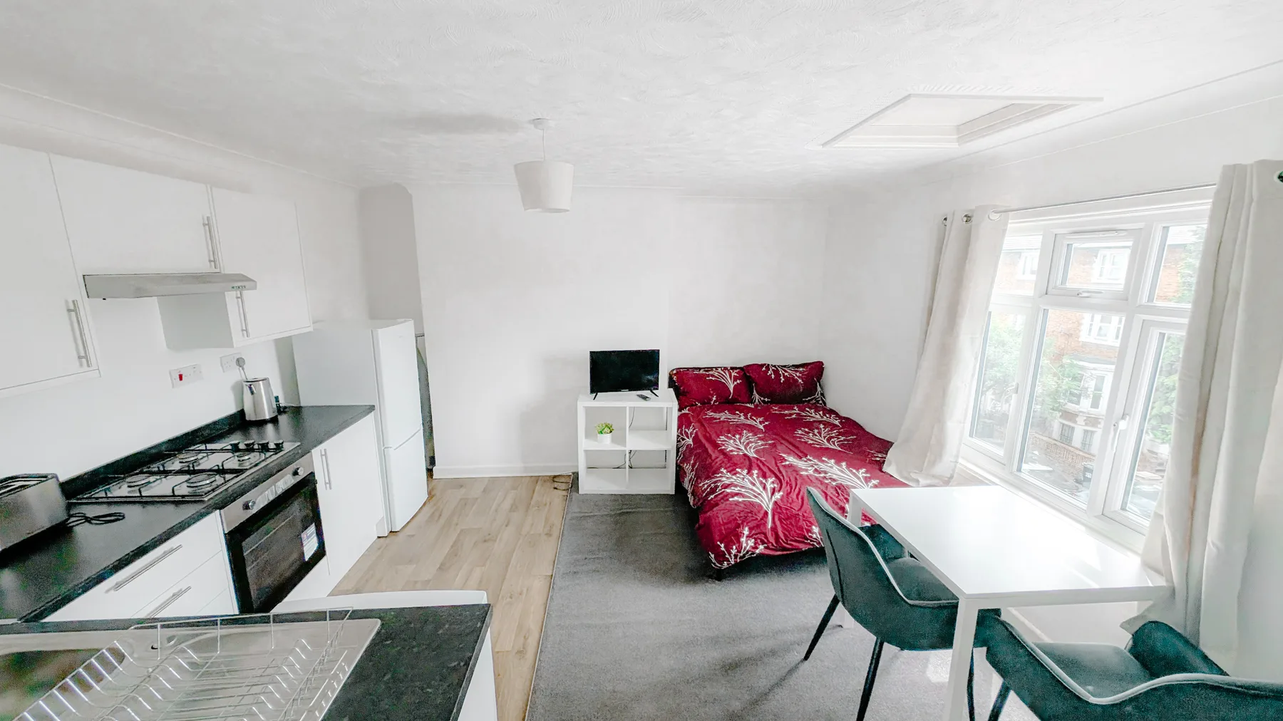 A bright room with a compact kitchen, a bed, and a small dining table.