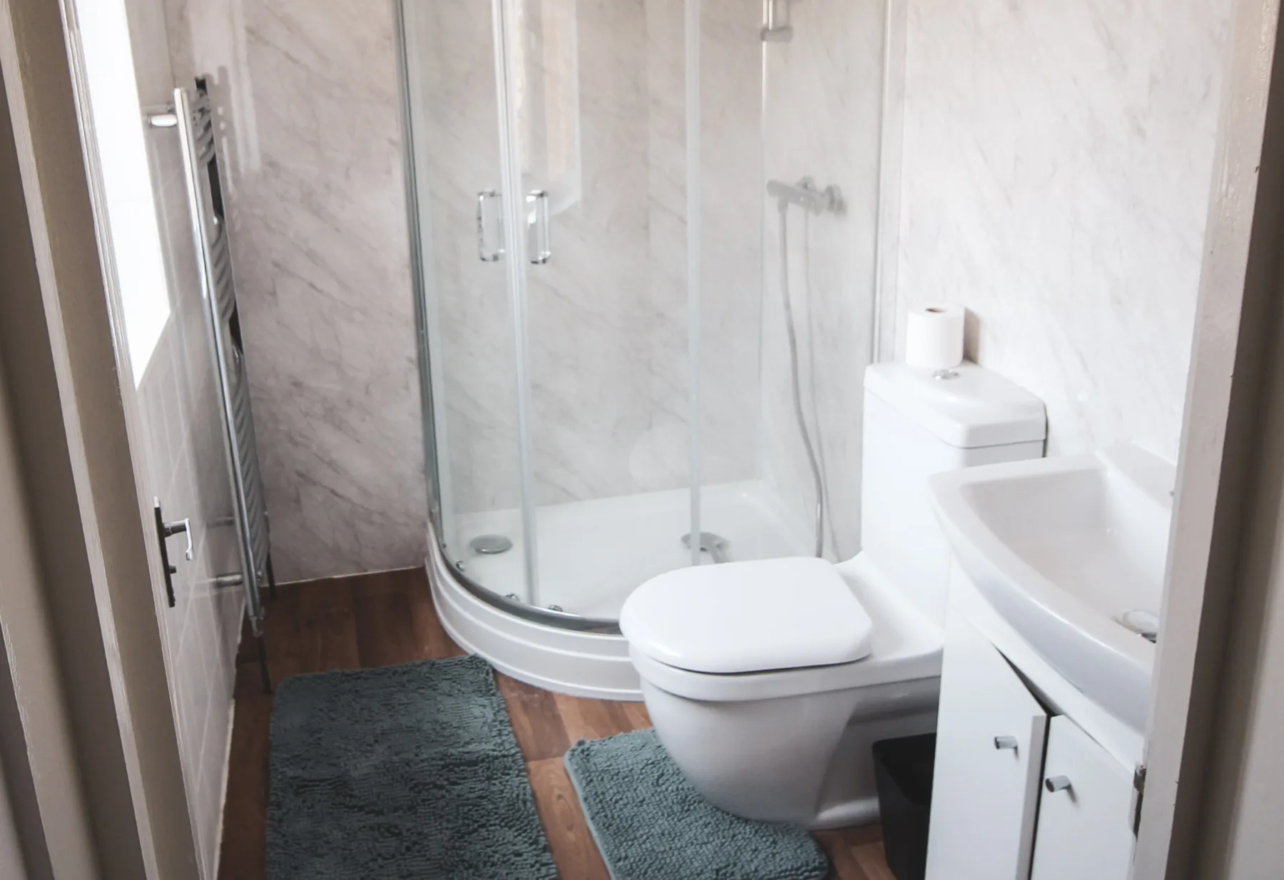 A bright bathroom with a curved glass shower, toilet, and sink.