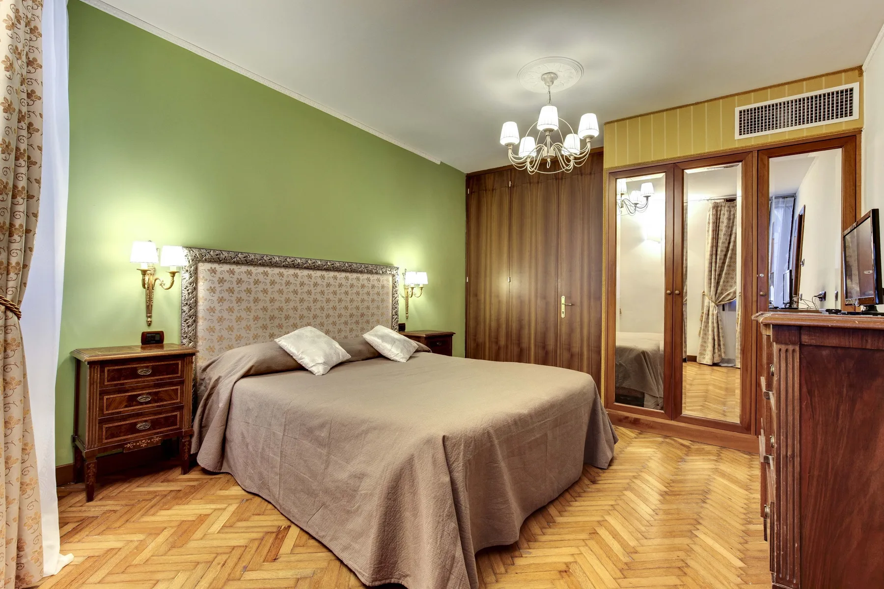 A bedroom with a large bed, green walls, and patterned wood flooring.