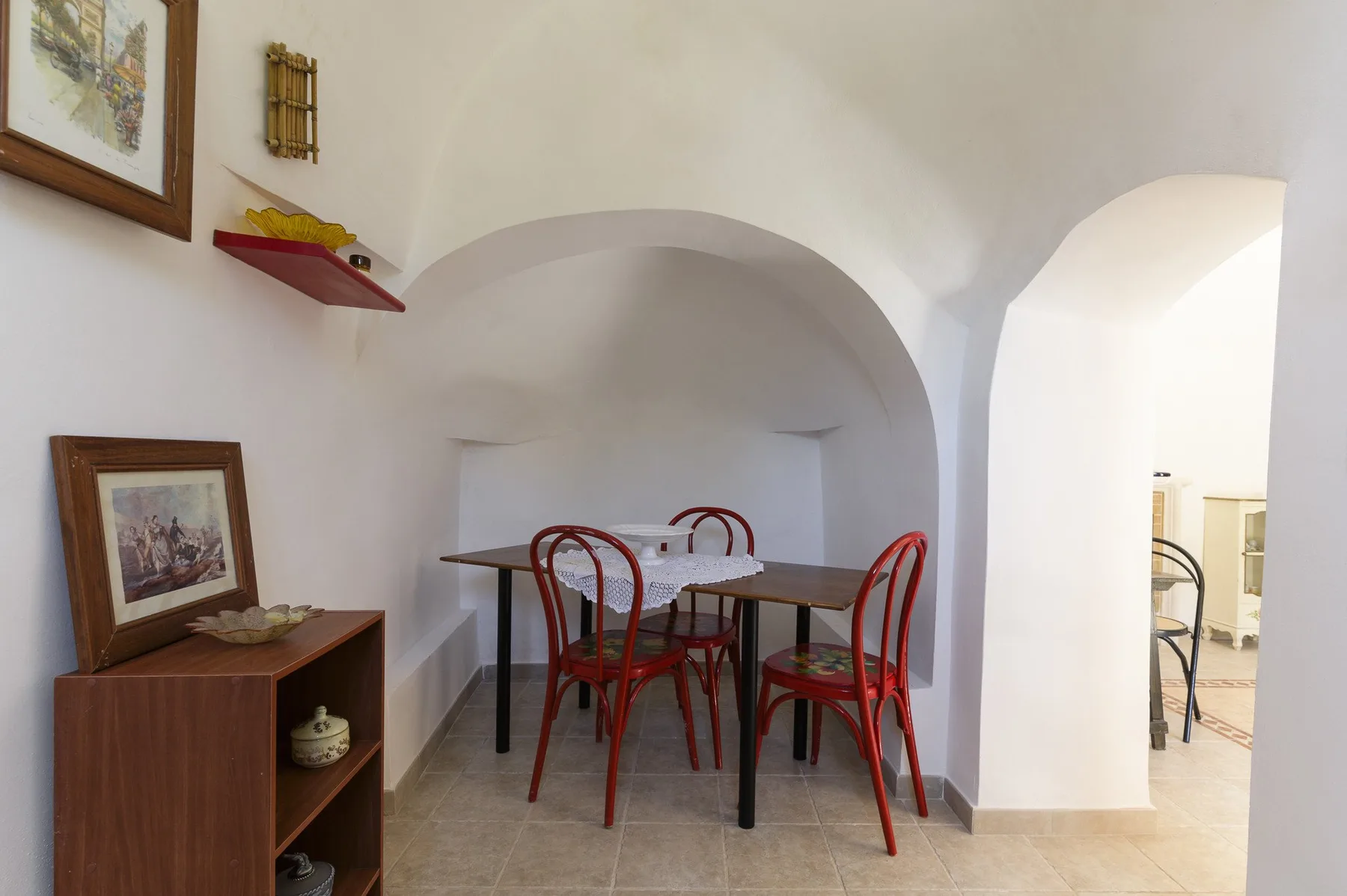 A dining area sits beneath a broad arch, with a table and red seating.