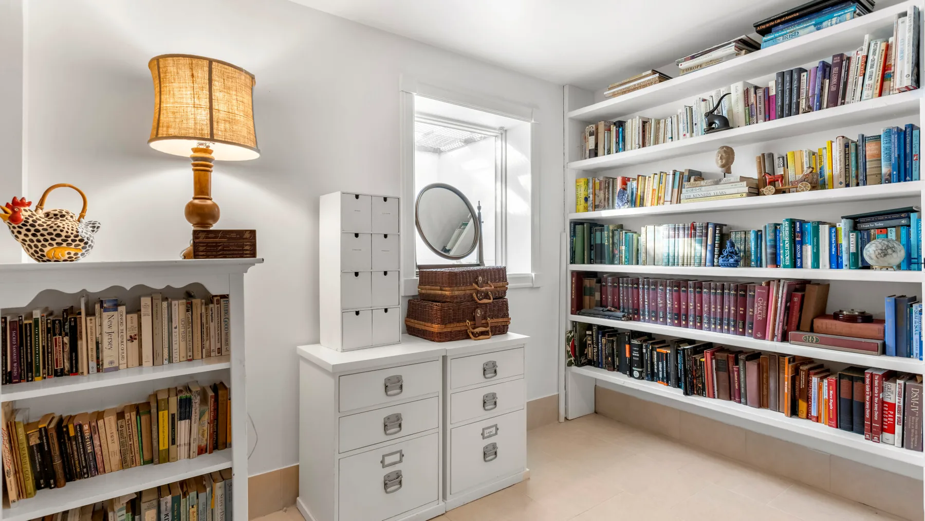 Una habitación luminosa con estanterías, una cómoda y un espejo.