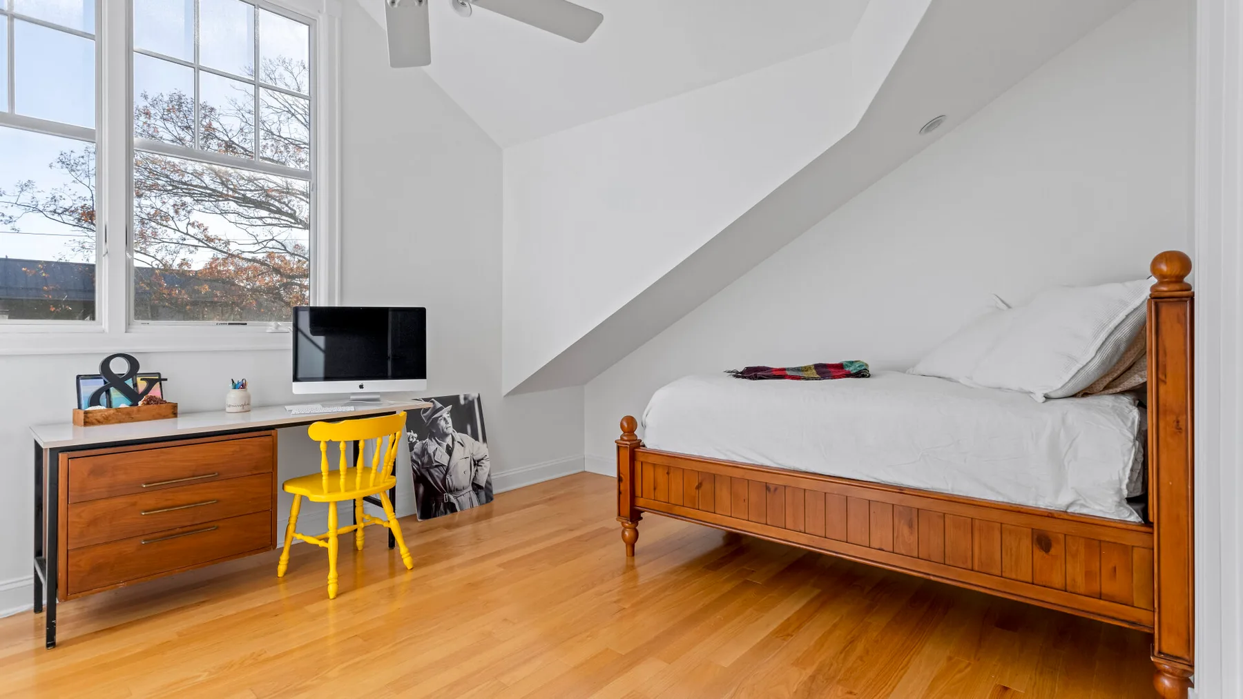 Un dormitorio luminoso con una cama de madera y un escritorio junto a las ventanas.