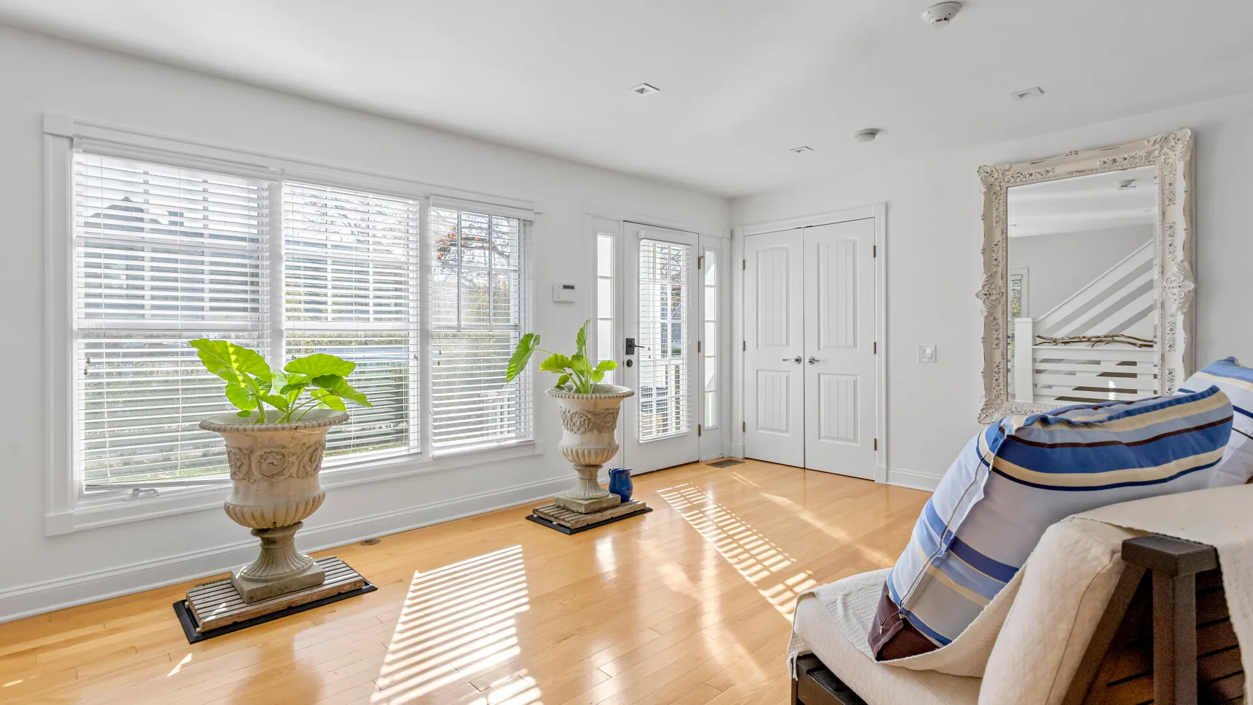 Una sala luminosa con ventanales, plantas en macetas y una zona de estar acolchada.