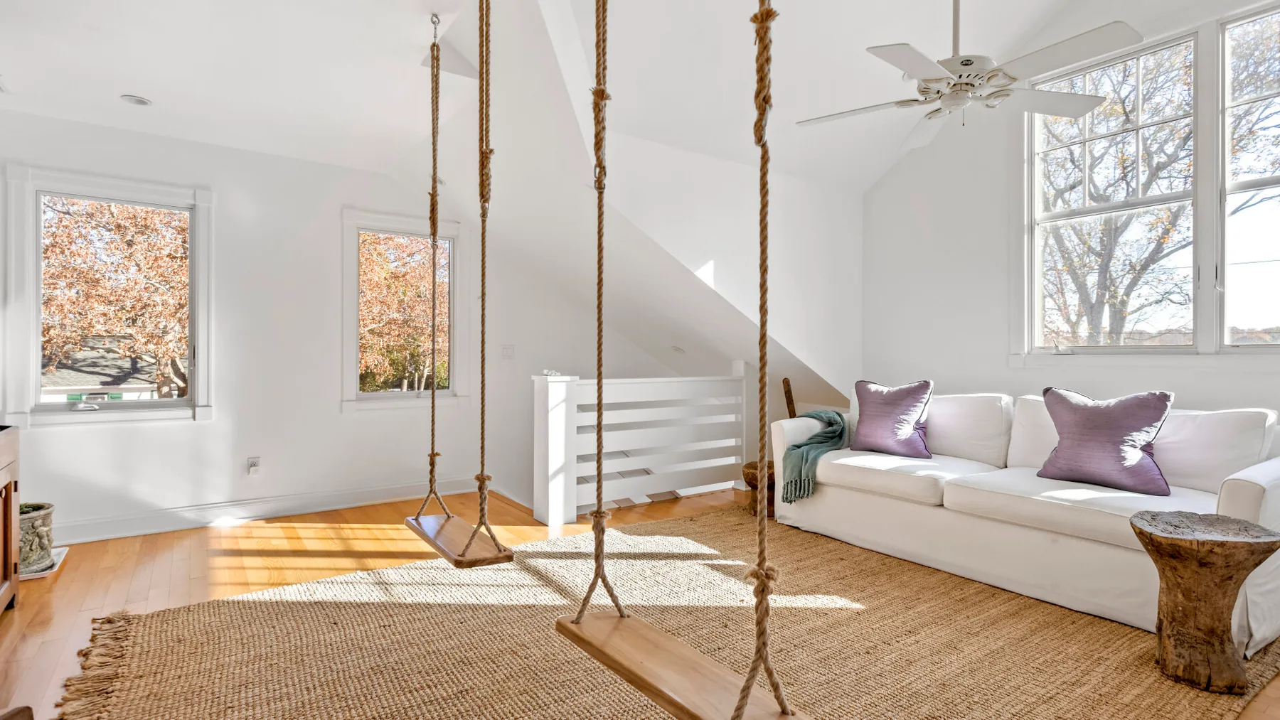 Una sala luminosa con un sofá blanco, una alfombra y columpios colgantes.