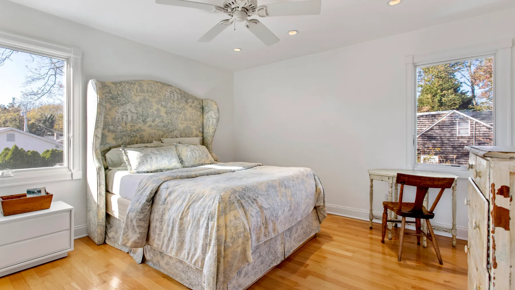 Un dormitorio luminoso con una cama, ventanas y un escritorio pequeño.