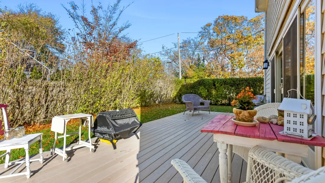 Una terraza exterior con asientos, una mesa y árboles alrededor.