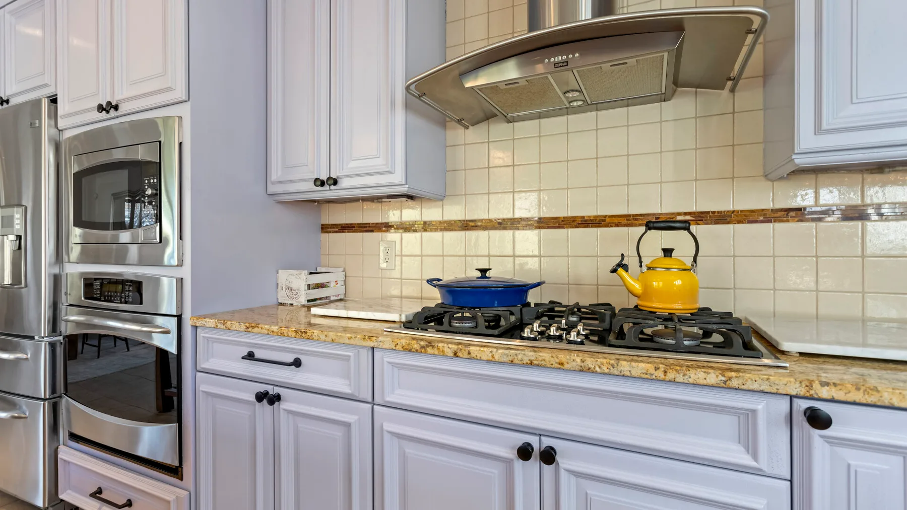 Una cocina con una estufa de gas, una tetera amarilla y gabinetes blancos.