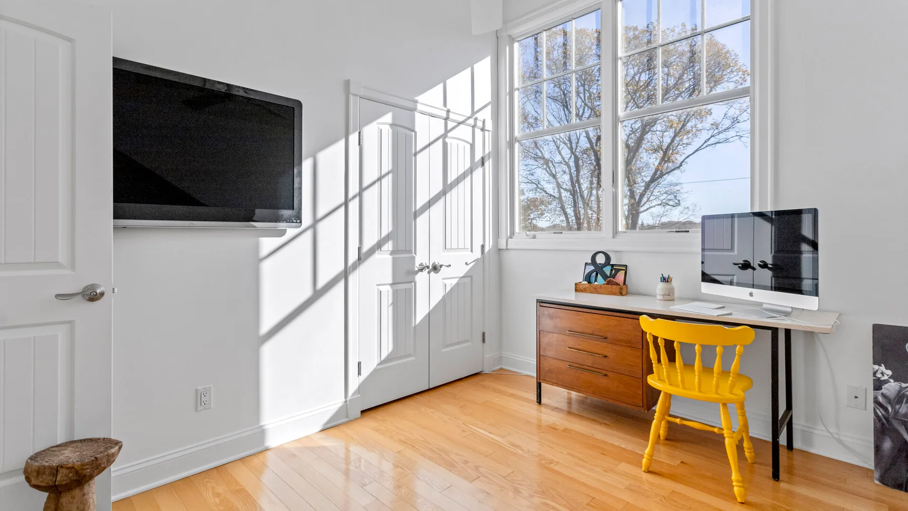 Una luminosa zona de escritorio con una computadora y una silla amarilla junto a grandes ventanas.