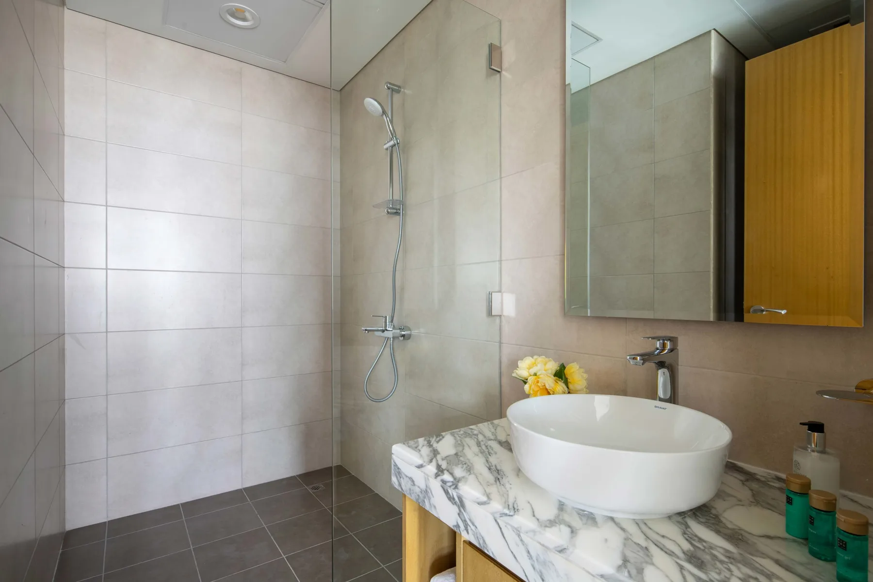 A tiled bathroom with a shower and a white basin on a marble-patterned counter.