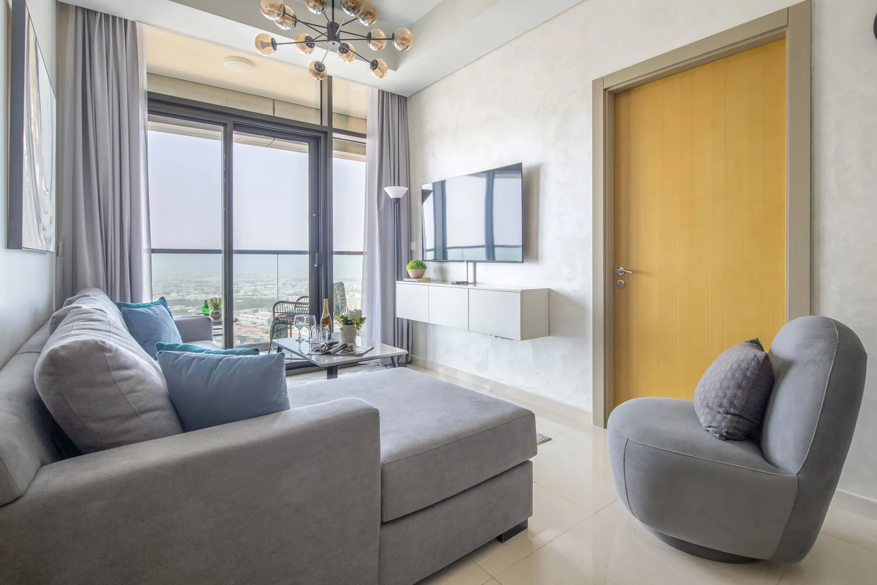 A living room with gray seating, a wall-mounted television, and large windows.