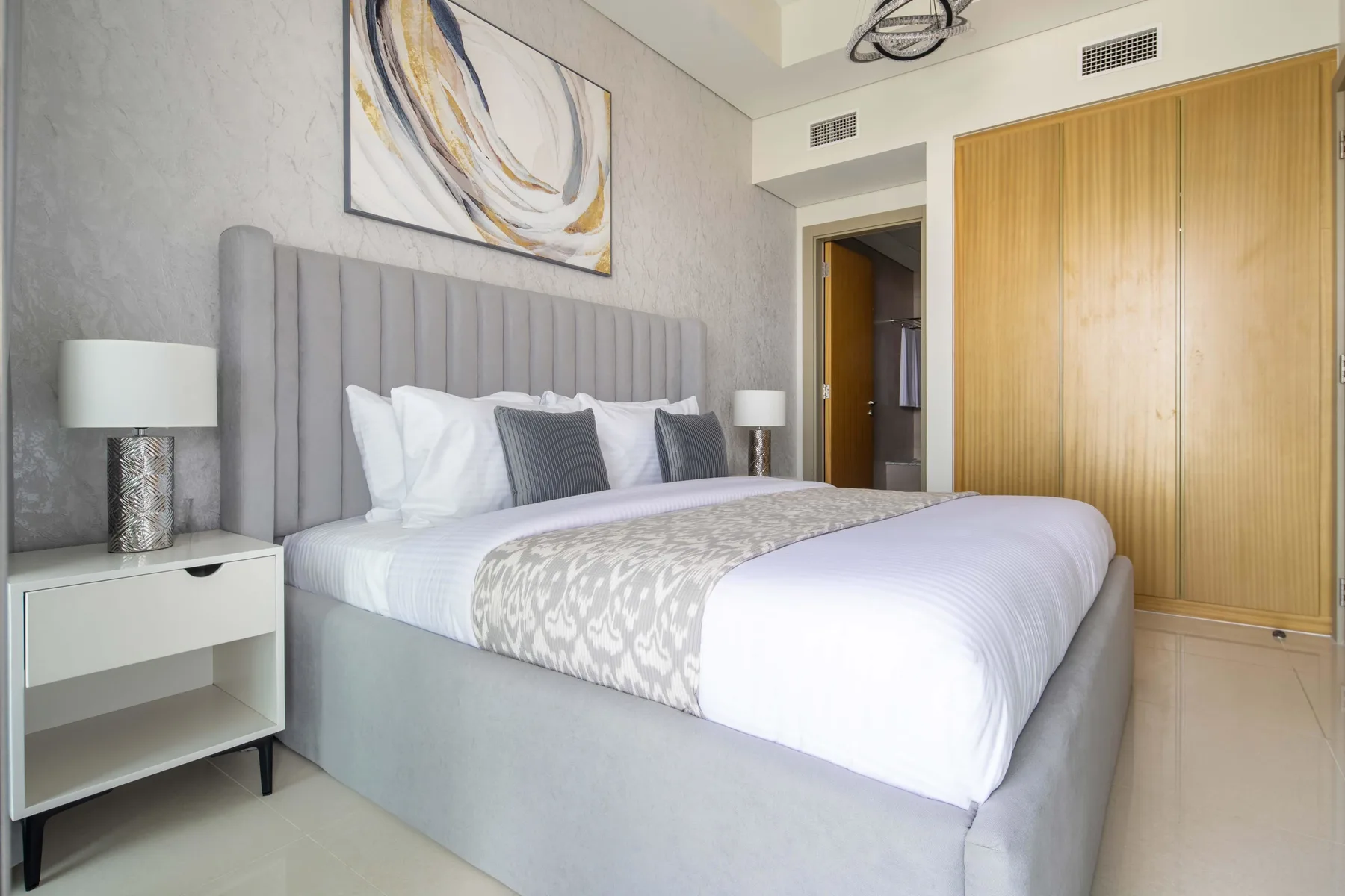 A bedroom with a neatly made bed, bedside tables, and abstract wall art.