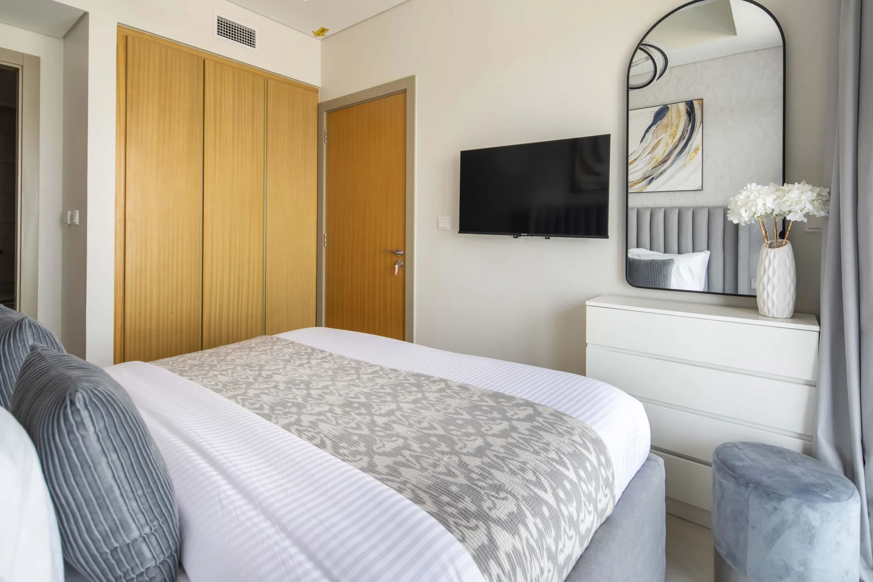 A bedroom with a neatly made bed, a wall-mounted television, and a dresser.