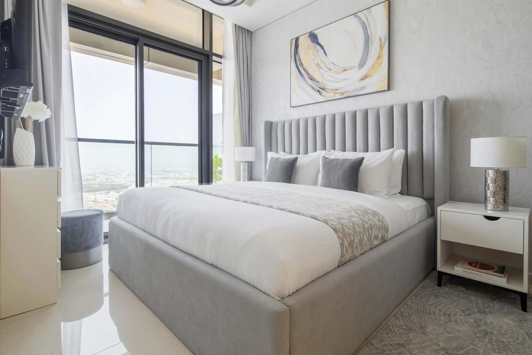 A bright bedroom with a large bed beside a floor-to-ceiling window.