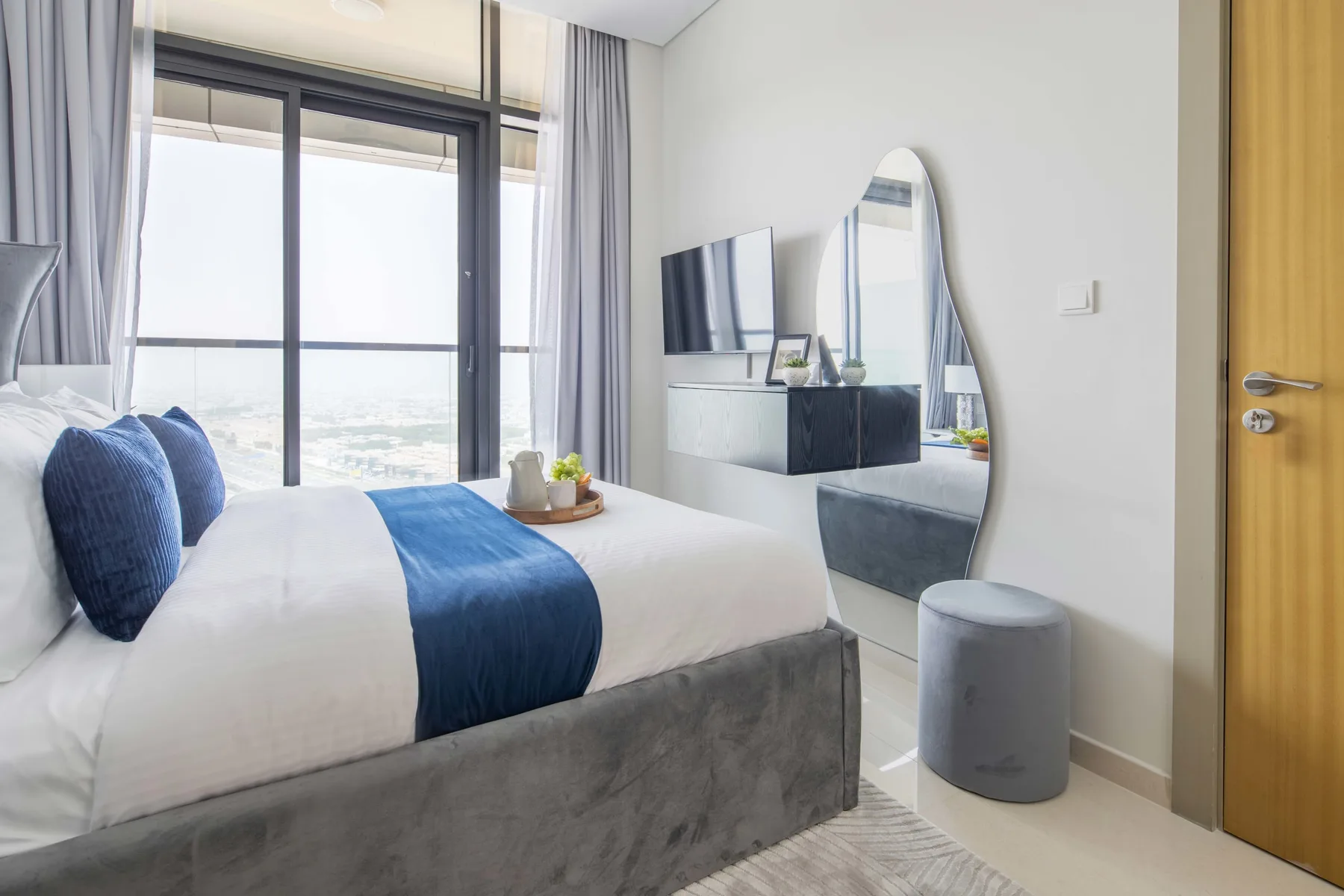 A bright bedroom with a bed, blue bedding, and a large window.