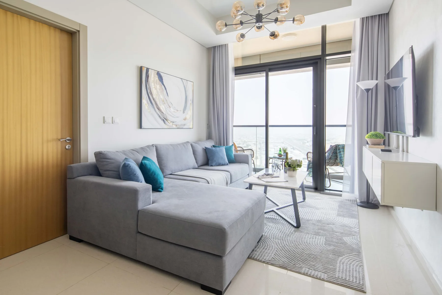 A bright living room with gray seating beside large windows and a glass coffee table.