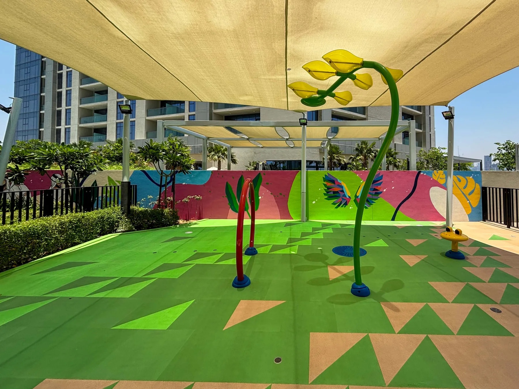 A colorful outdoor play area has patterned green flooring and oversized flower sculptures.