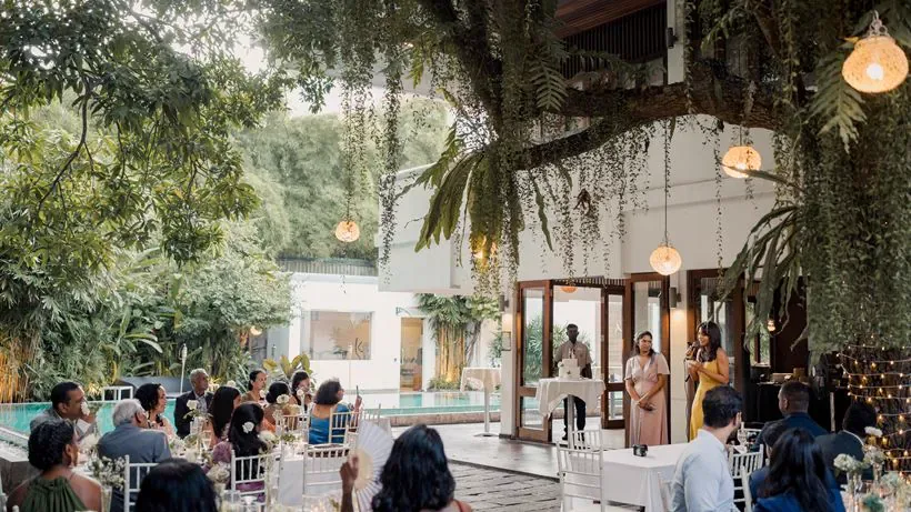 Huéspedes sentados para una recepción en el jardín bajo lámparas colgantes.