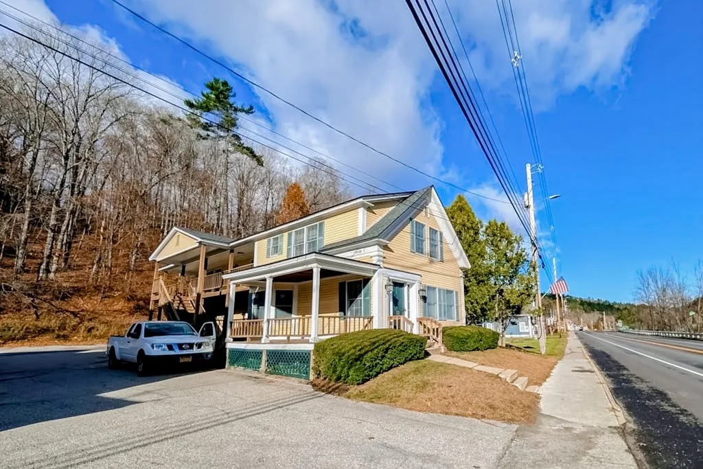 A two-story house stands beside a paved driveway and roadside sidewalk.