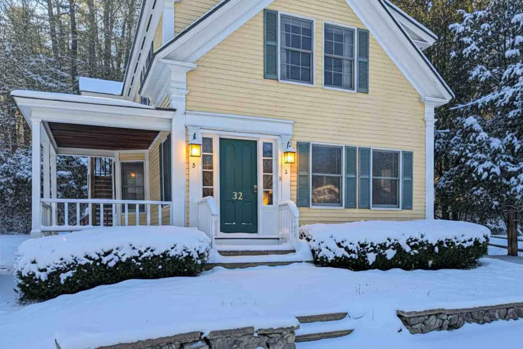 A yellow house stands in a snowy yard, with a covered porch and green front door.