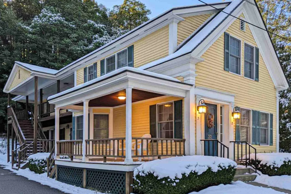 A snow-covered yellow house with a lit covered porch.
