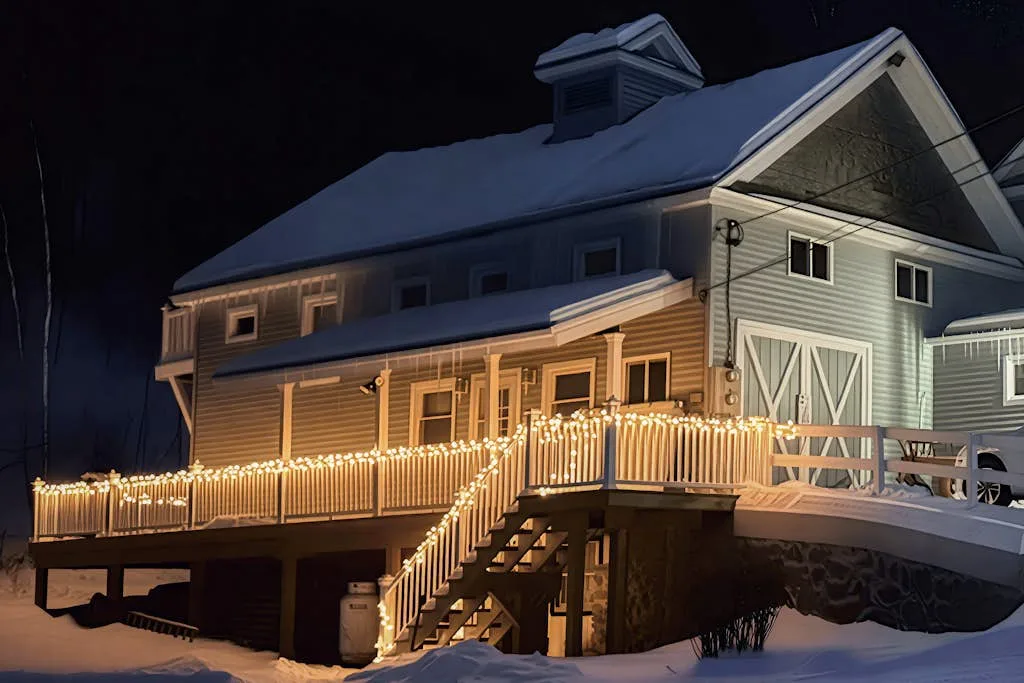 A large barn-style building at night, with warm lights along the deck and stairs.