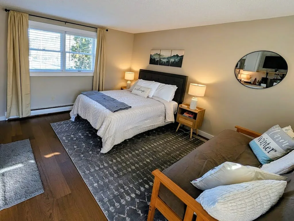 A bedroom with a neatly made bed, a window, and a seating area.