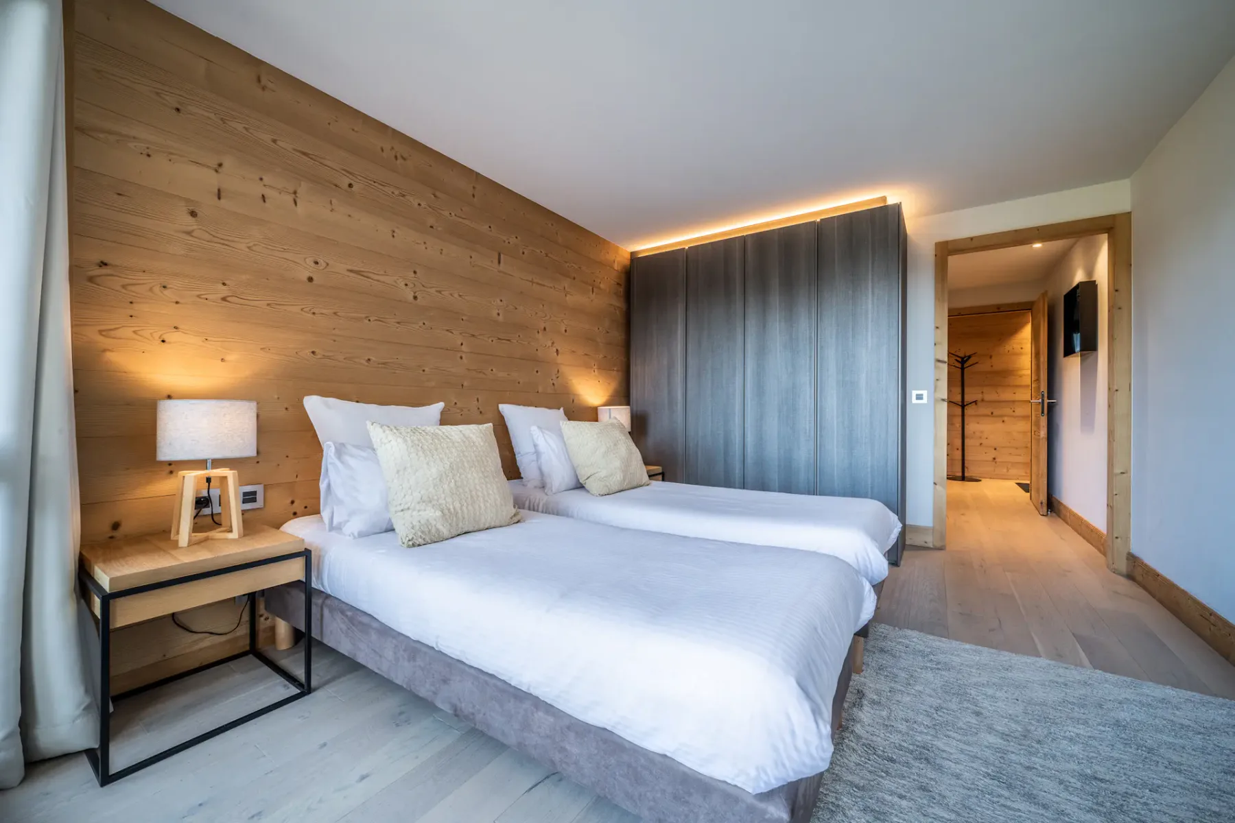 Un dormitorio con dos camas, una pared de madera y una puerta al pasillo.