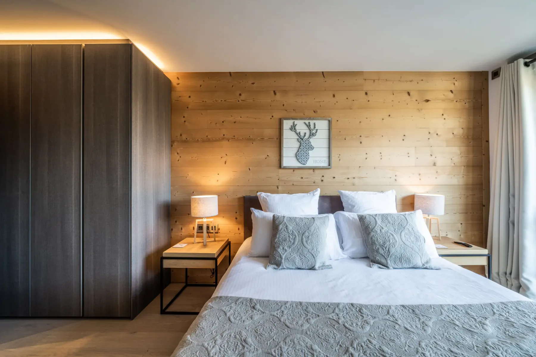 Un dormitorio con una cama bien hecha, mesitas de noche y paredes revestidas de madera.