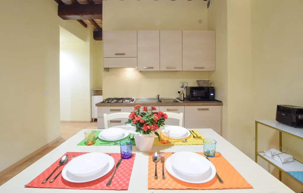 A dining table set with plates sits in front of a compact kitchen.
