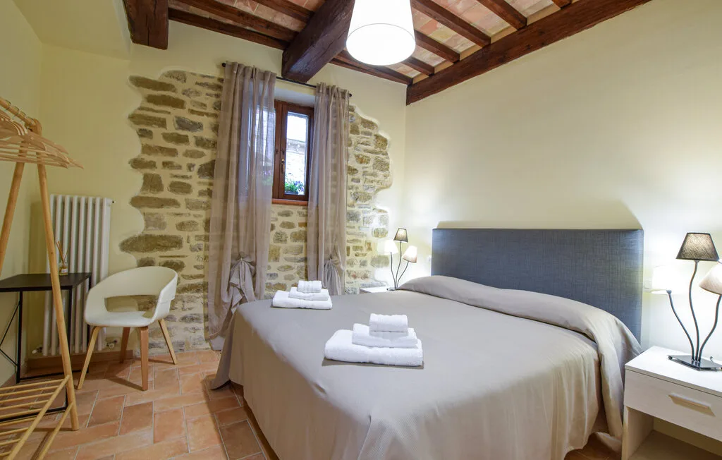A bedroom with a large bed, exposed ceiling beams, and a stone accent wall.