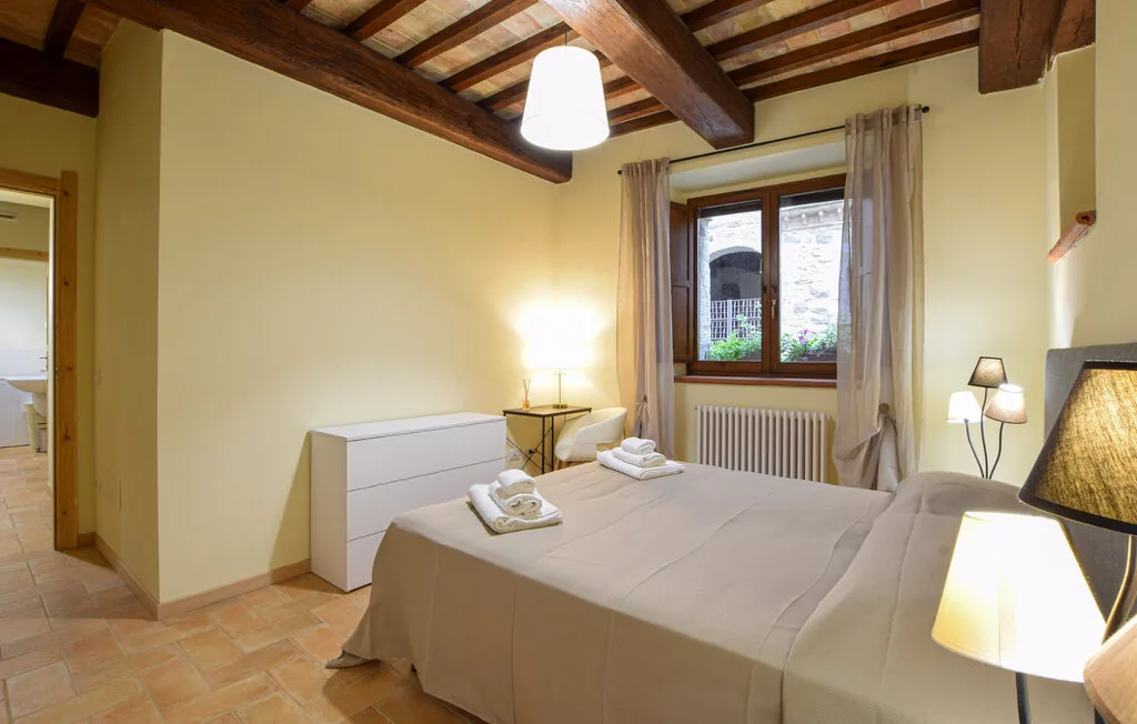 A bedroom with a neatly made bed and a window overlooking greenery.