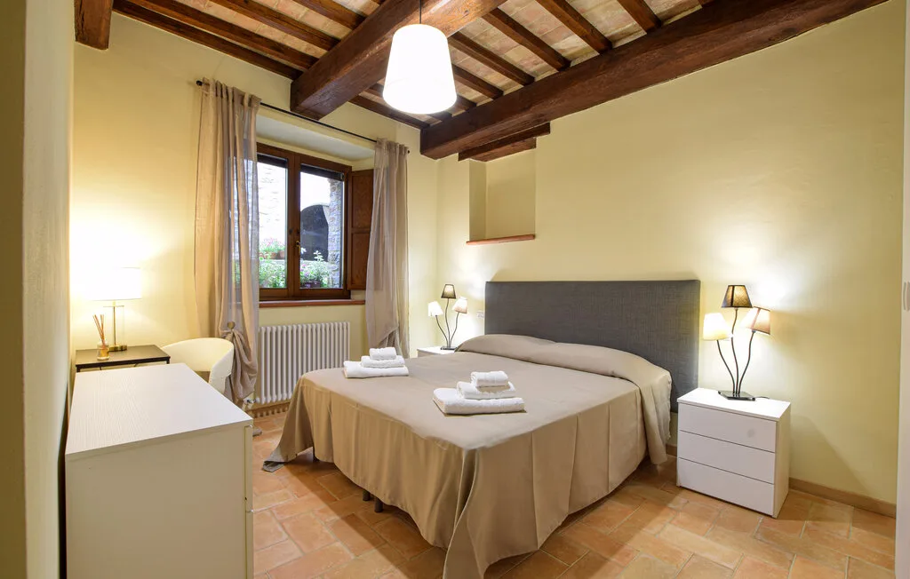 A bedroom with a double bed, bedside tables, and a window beneath exposed ceiling beams.