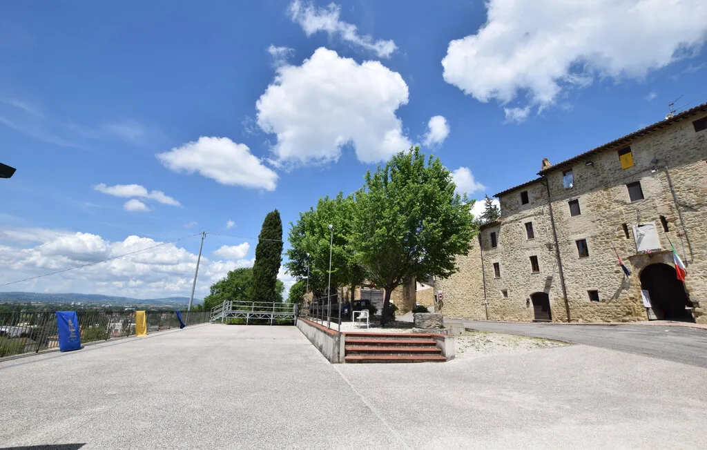 A paved outdoor courtyard beside a stone building, with trees and distant hills.