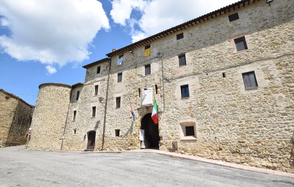 A large stone building with several windows stands beside an open paved area.