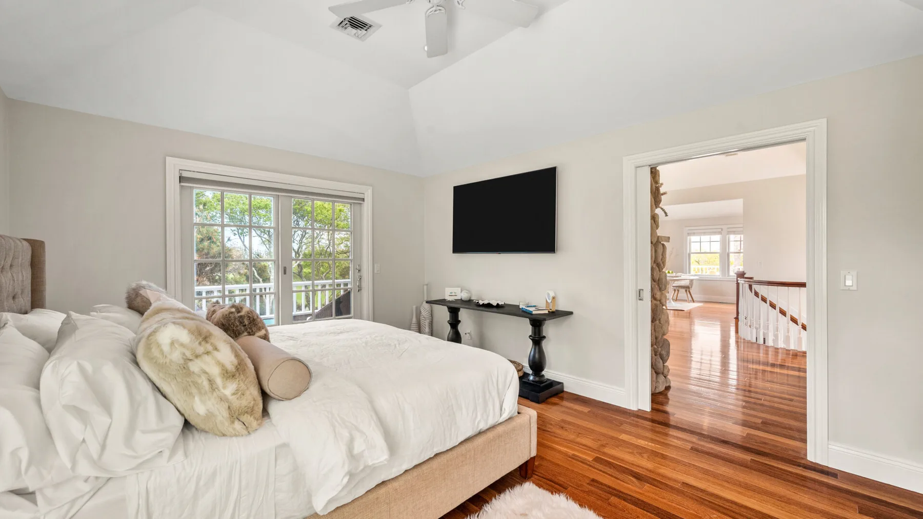 Un dormitorio con una cama, un televisor montado en la pared y ventanas con vista a un balcón.