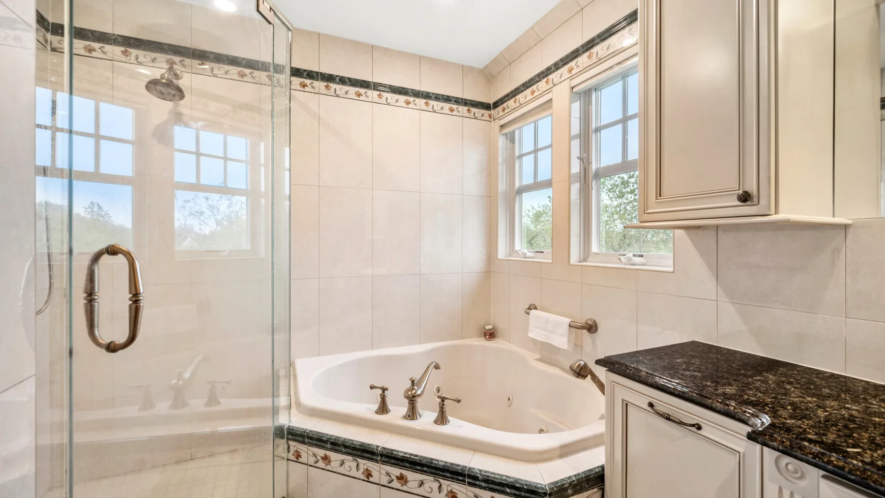 Un baño luminoso cuenta con una ducha de vidrio, una bañera y ventanas grandes.