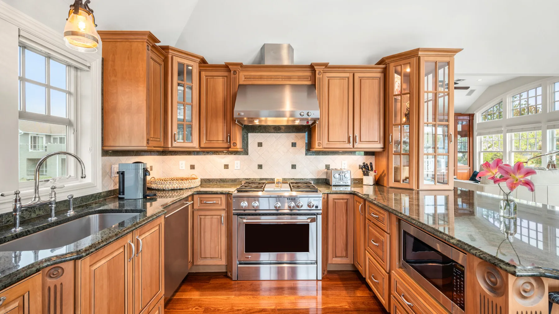 Una cocina amplia con gabinetes de madera, encimeras oscuras y electrodomésticos de acero inoxidable.