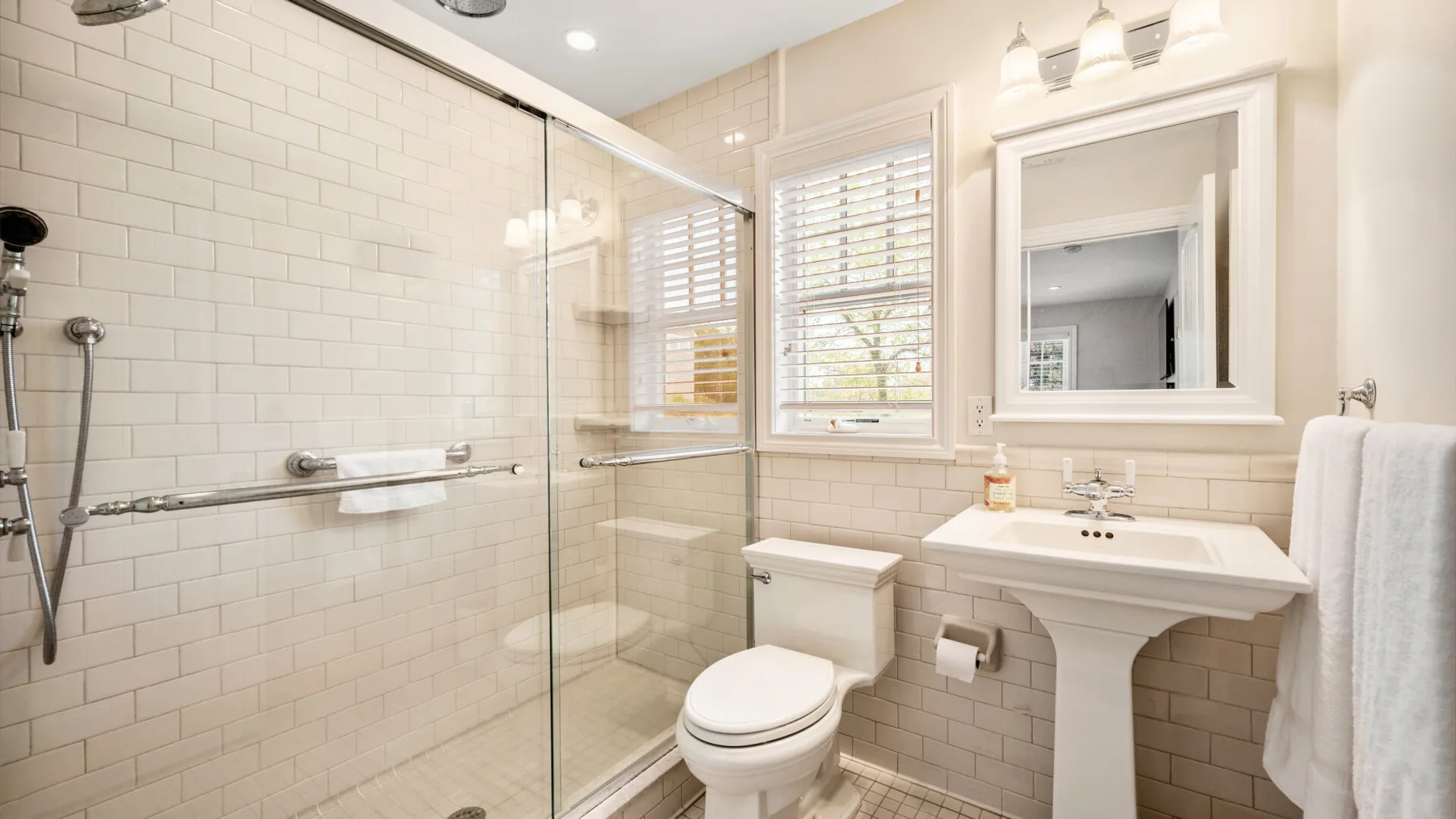 Un baño luminoso con ducha de cristal, inodoro y lavabo con pedestal.