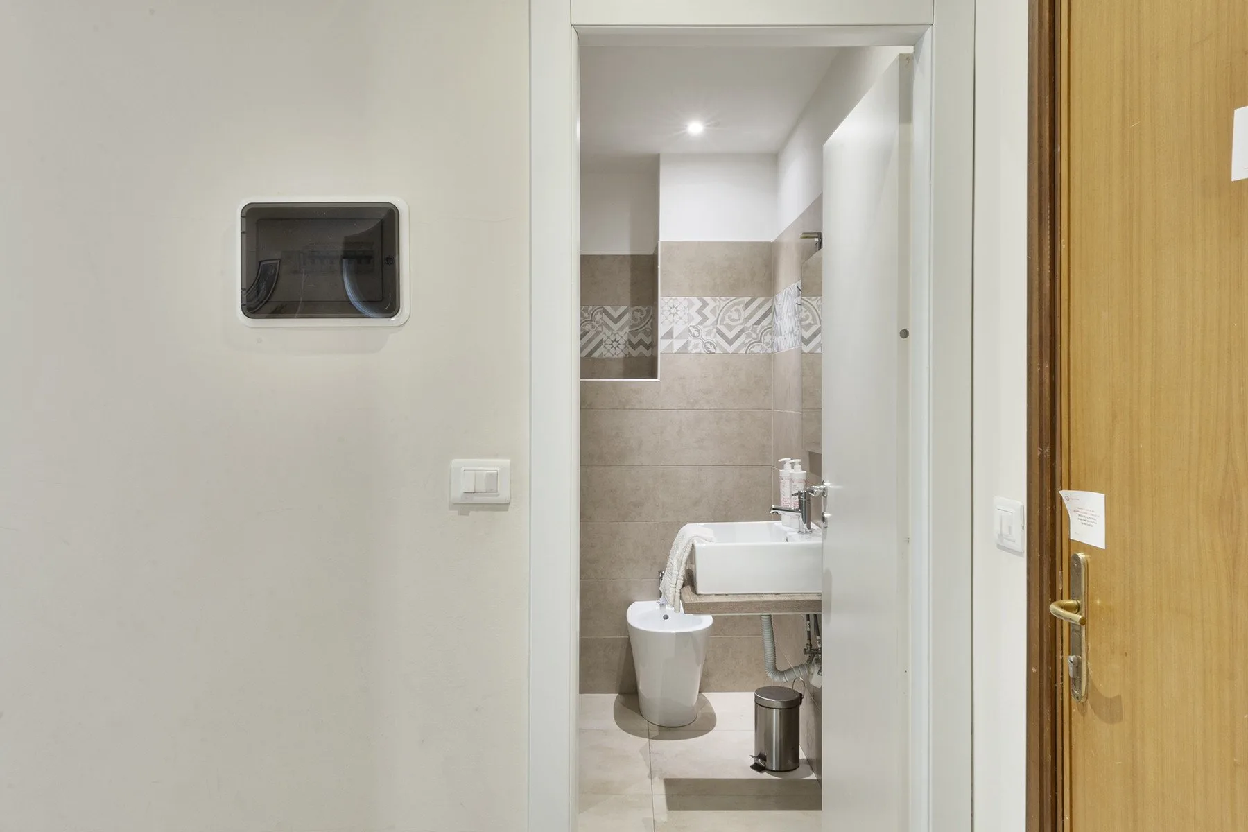 A bathroom doorway reveals a sink, toilet, and tiled walls.