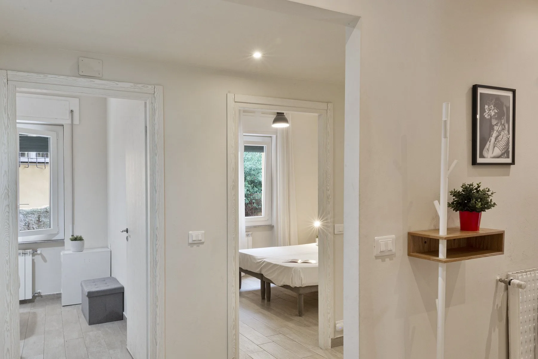 A bright hallway opens onto two rooms, with a bed visible in the center doorway.