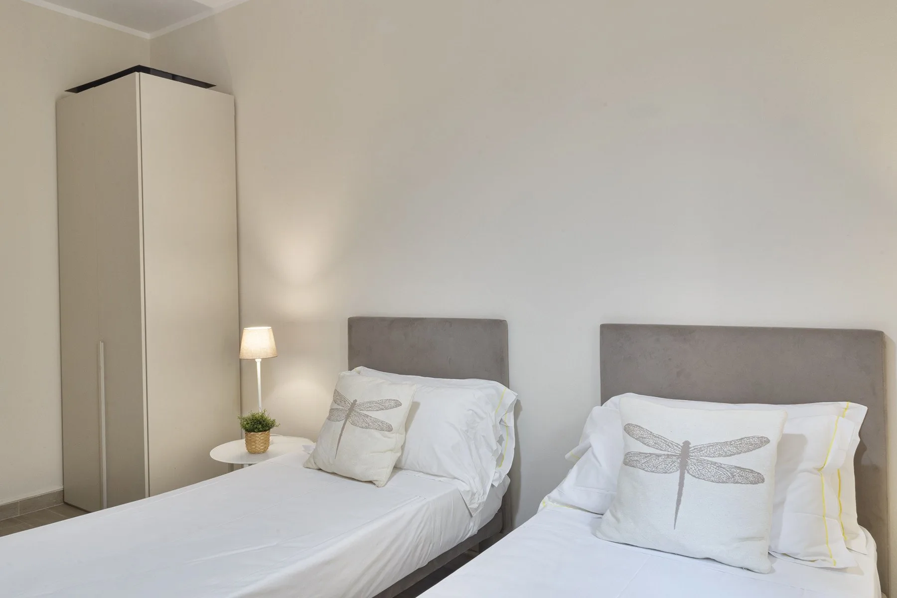 A bedroom with two beds, white bedding, and a tall wardrobe.