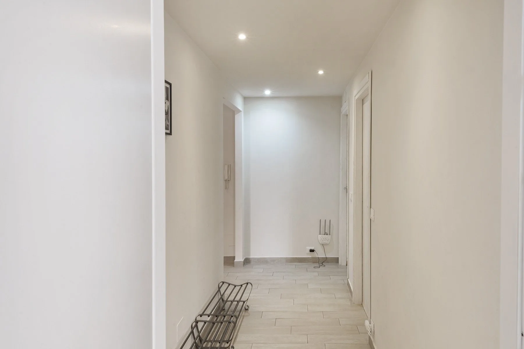 A bright hallway with recessed ceiling lights and a narrow metal shoe rack.