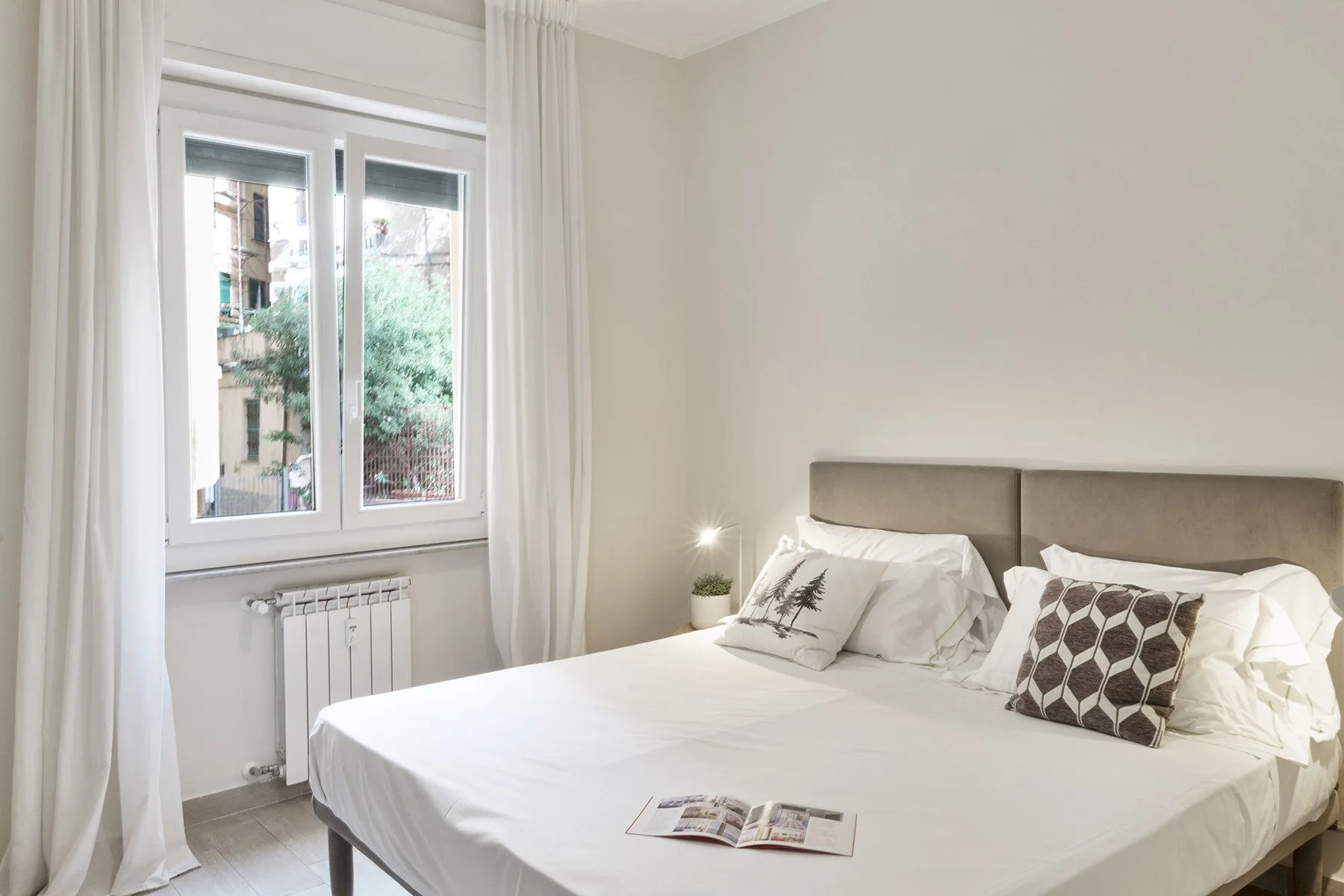 A bright bedroom with a double bed and a window overlooking greenery.