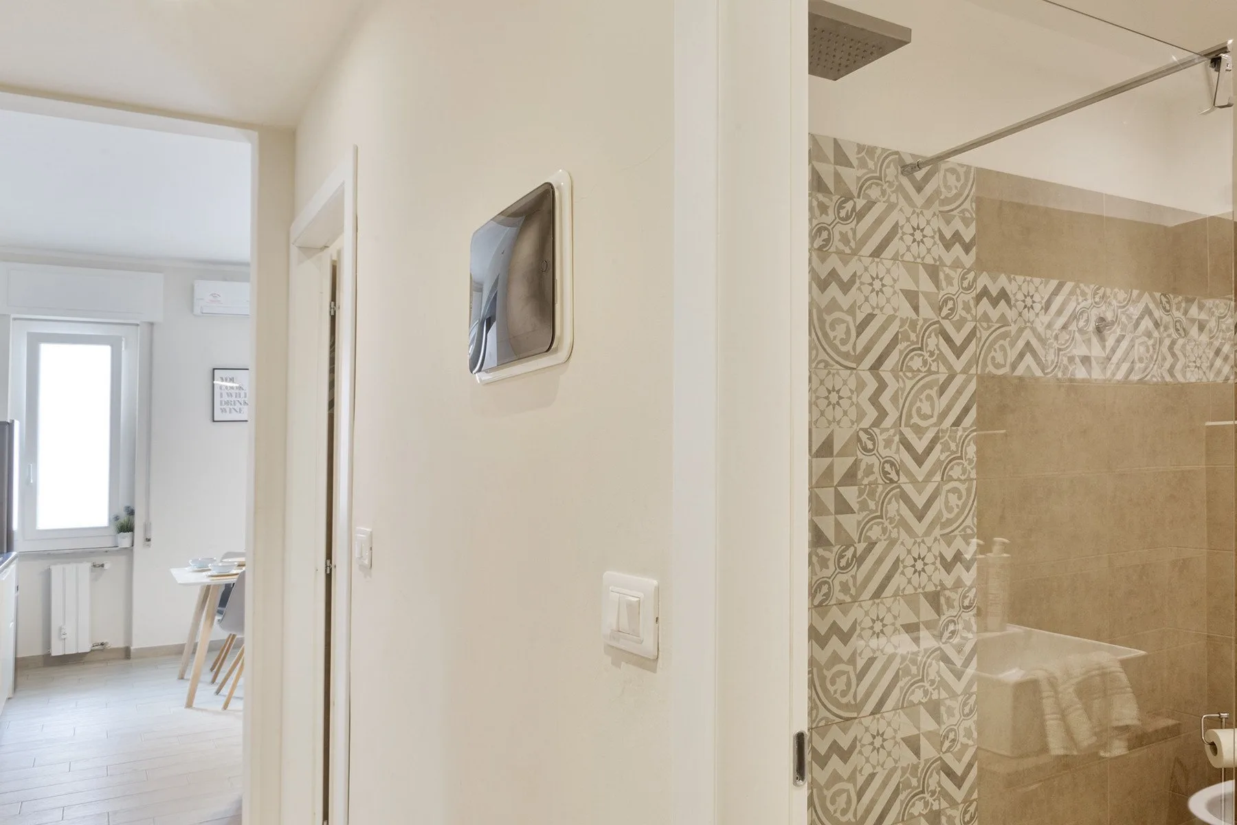 A hallway opens onto a bathroom with patterned wall tiles and a glass shower screen.