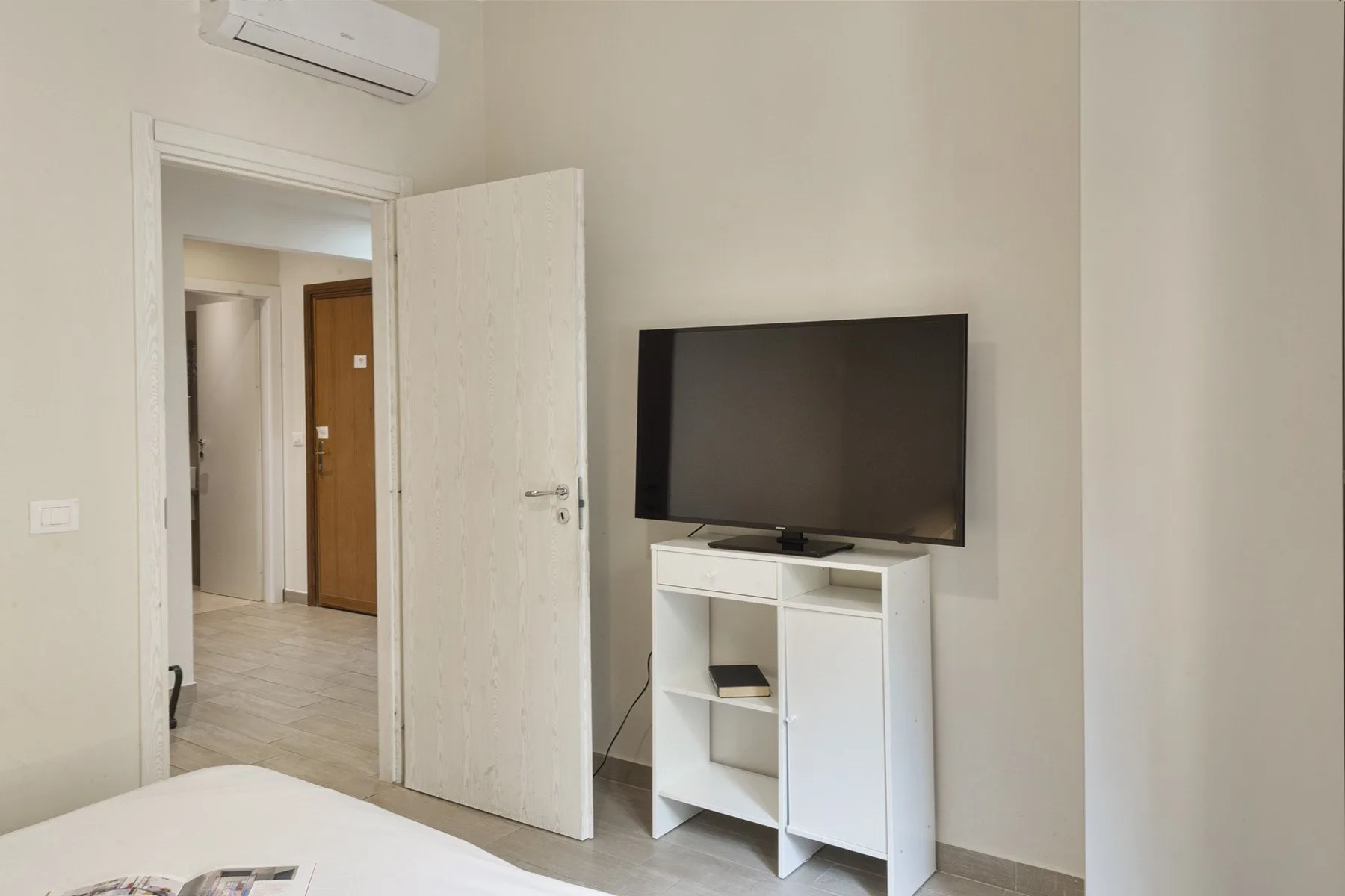 A bedroom with a television on a white stand beside an open doorway.